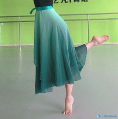 a woman standing on one leg with her legs crossed in the air, wearing a green skirt and black top