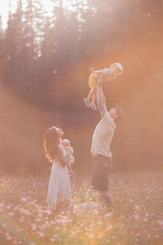 a man and woman are holding their baby up in the air as they walk through a field