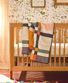 a baby's crib with a blanket on it in front of a floral wallpaper