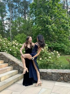 two young women are dancing on the steps in front of some trees and bushes, one is holding another woman's leg