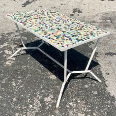 a white table with multicolored dots on it sitting in the middle of a parking lot