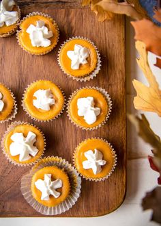 small cupcakes with white frosting on a wooden cutting board next to autumn leaves