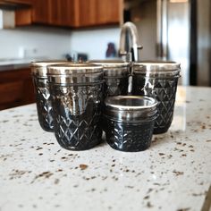 three black glass cups sitting on top of a counter next to a faucet