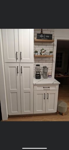 a kitchen with white cupboards and shelves on the wall next to a coffee maker