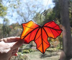 a hand holding up a stained glass leaf ornament in front of a tree