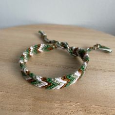 a close up of a rope bracelet on a wooden table with white and green beads