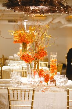 an arrangement of flowers in vases and glasses on a table with white clothed tables