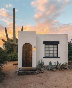 a small white house with cactus and cacti in the foreground at sunset