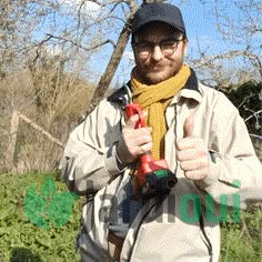 a man with glasses and a hat holding a red tool in his hands while standing next to some trees