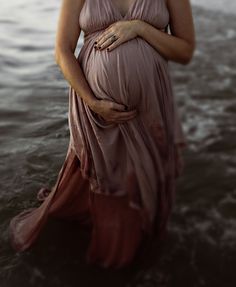 a pregnant woman is standing in the water with her belly wrapped around her waist and wearing a pink dress