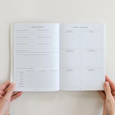 two hands holding an open book on top of a white table with the pages marked out