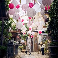 a woman walking down a street with lots of pink and white lanterns hanging from the ceiling