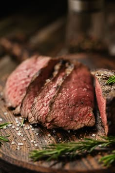 steak sliced up on a wooden cutting board with rosemary sprigs and seasoning