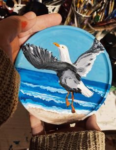 a person holding up a painted plate with a bird flying over the ocean on it