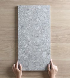 two hands holding up a piece of paper on top of a wooden table with wood flooring