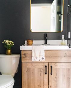 a white toilet sitting next to a wooden cabinet under a bathroom mirror with a gold framed mirror above it