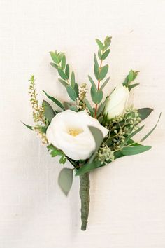 a boutonniere with white flowers and greenery on a white wall background