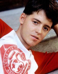 a young man sitting on the ground wearing a red and white shirt