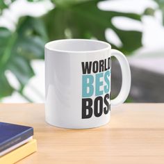 a white coffee mug with the words world's best boss on it sitting next to a book