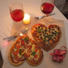 two heart shaped pizzas sitting on top of a table next to glasses of wine