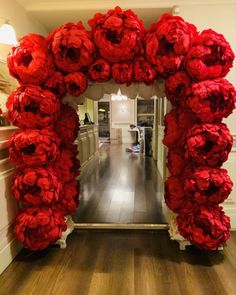 an archway made out of red paper flowers in a hallway with wood floors and white walls