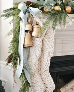 christmas stockings hanging from a mantel decorated with greenery and bells