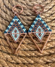 two triangle shaped beaded earrings sitting on top of a pile of roped material