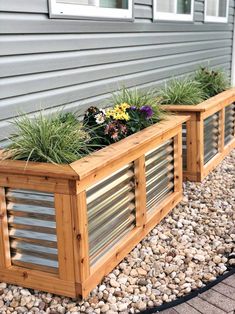 two wooden planters filled with plants next to a gray house and graveled walkway