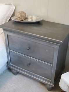 a gray dresser with two drawers and a plate on top of it next to a bed