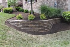 a brick retaining wall in front of a house with green grass and shrubs around it