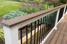 a wooden deck with white railing and black iron handrails in front of a garden