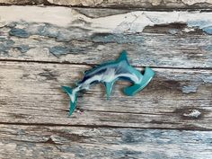 a blue and white fish shaped brooch sitting on top of a wooden table next to a piece of wood