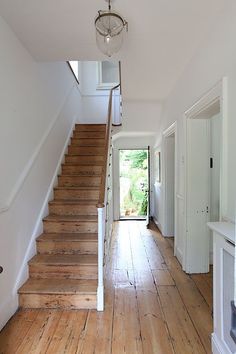 an empty hallway with wooden floors and white walls, leading up to the second floor