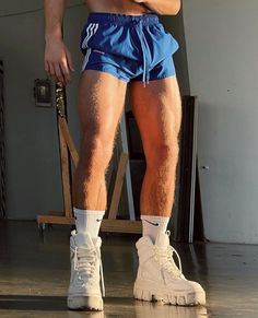 a man in blue shorts and white socks standing on a chair with his arms crossed