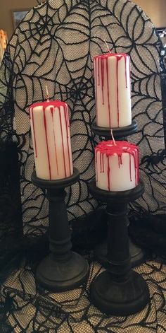 three candles with blood running down them sitting on a lace covered tablecloth in front of a black net