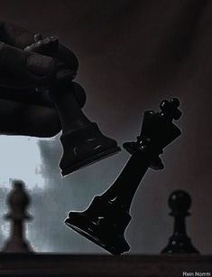 a hand holding a black chess piece next to two pieces of white and black chess