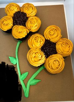 cupcakes decorated with yellow icing and flowers on top of a brown paper