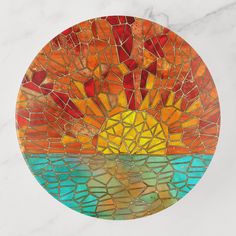 a round glass plate with an orange and yellow sun in the center on a white marble surface