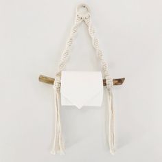 a white toilet paper holder hanging from a rope with two wooden sticks attached to it