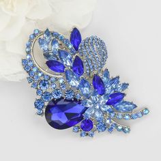 a brooch with blue and clear stones on it next to a white flower ornament