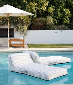 an outdoor lounge chair sitting on top of a swimming pool next to a white umbrella