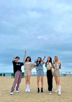 four young women standing on top of a sandy beach next to the ocean with their arms in the air