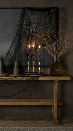 candles are lit on a table in front of a painting with black and gold accents