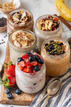 four jars filled with different types of food on top of a wooden cutting board next to bananas and strawberries