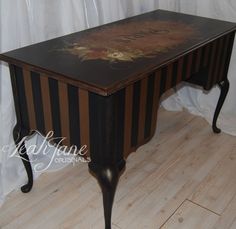 an antique desk painted black and brown with flowers on the top, sitting in front of a white curtain