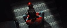 a person in a red spider suit sitting on the floor with their hands behind their head