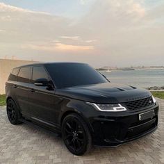 a black range rover parked in front of a body of water on a brick walkway