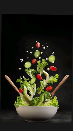 a salad with lettuce, tomatoes and cucumbers is tossed in the air