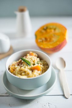 a white bowl filled with food next to a spoon and an orange in the background