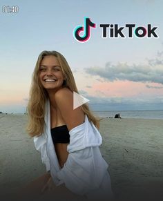 a woman sitting on top of a sandy beach next to the ocean with tiktok logo